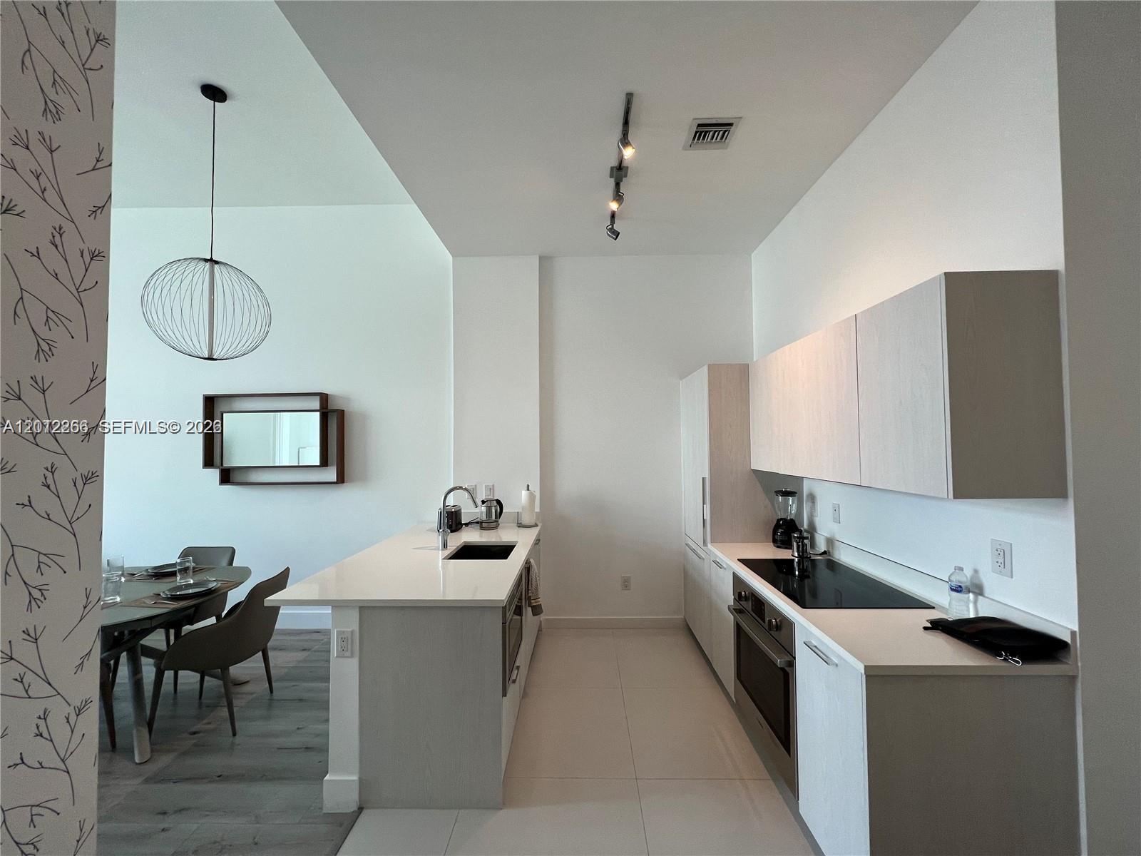 A modern kitchen features light wood cabinetry, white countertops, and an adjacent dining area — 501 NE 31st St # 404, Miami FL 33137, MIAMI, FL