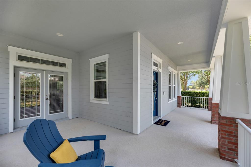 A covered porch features gray siding, a blue front door, and a blue Adirondack chair — 14103 BARRINGTON STOWERS DRIVE, LITHIA, FL