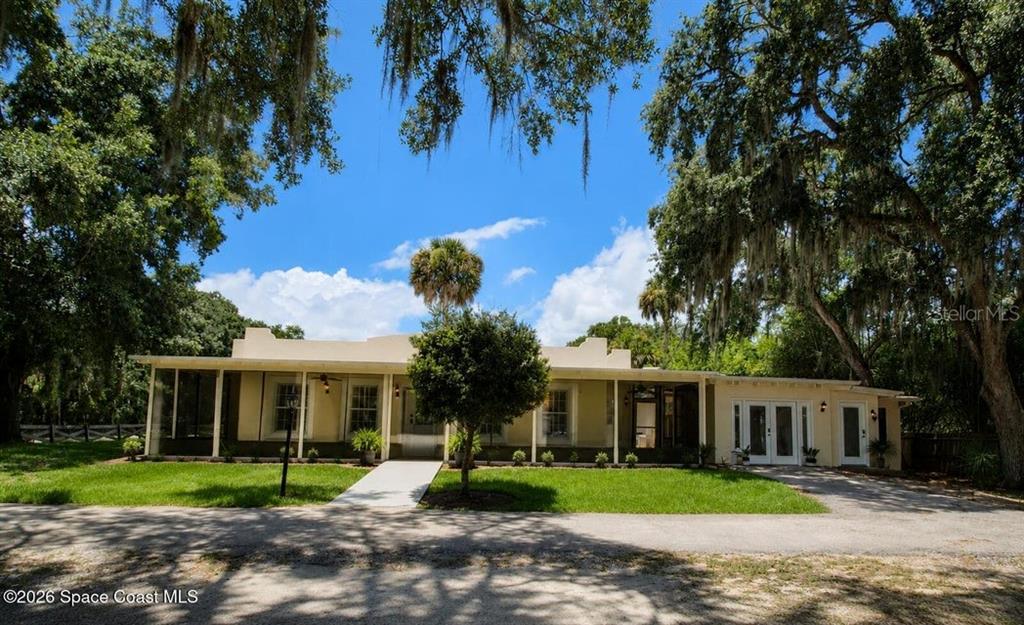 A single-story house with a screened porch and a flat roof sits among large trees — 140 BELLEWOOD STREET, TITUSVILLE, FL