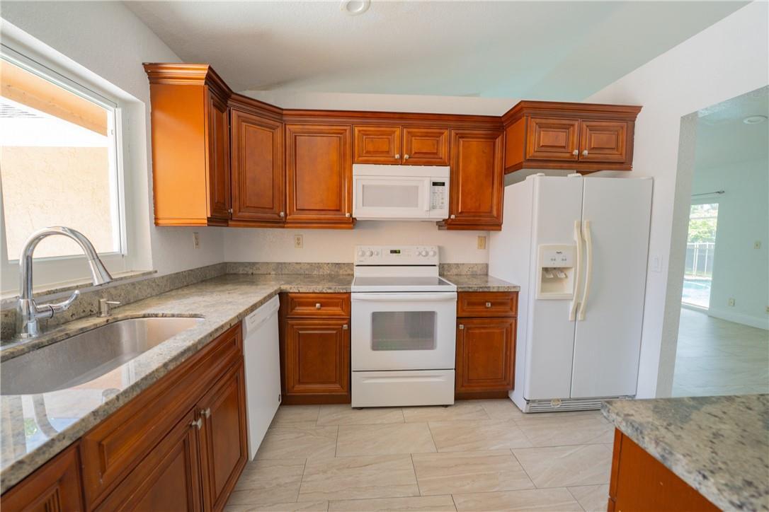 A kitchen features wood cabinets, granite countertops, white appliances, and light-colored tile flooring — 5332 NW 29th Court, Margate FL 33063, MARGATE, FL