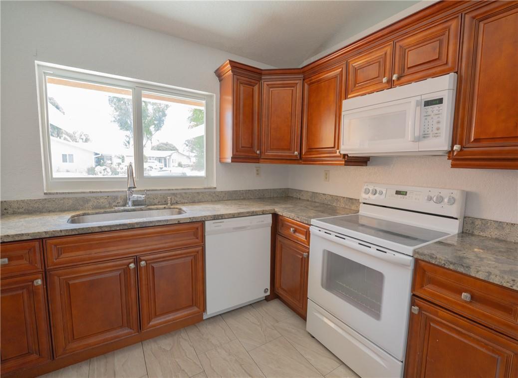 A kitchen features wood cabinets, granite countertops, a white stove, and a stainless steel sink — 5332 NW 29th Court, Margate FL 33063, MARGATE, FL