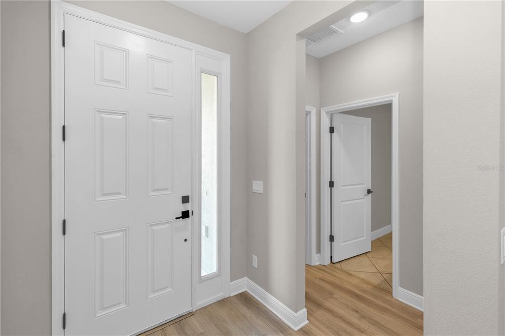 An entryway features a white front door with a sidelight, light wood flooring, and neutral walls — 790 HYPERION DRIVE, DEBARY, FL