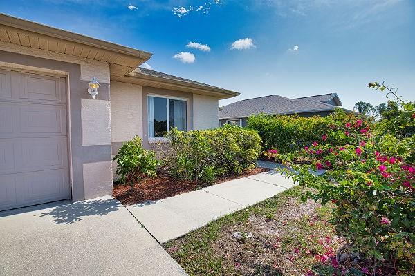A beige house exterior features a garage, a concrete walkway, and a flowering bougainvillea bush — 116 ALBATROSS ROAD, ROTONDA WEST, FL