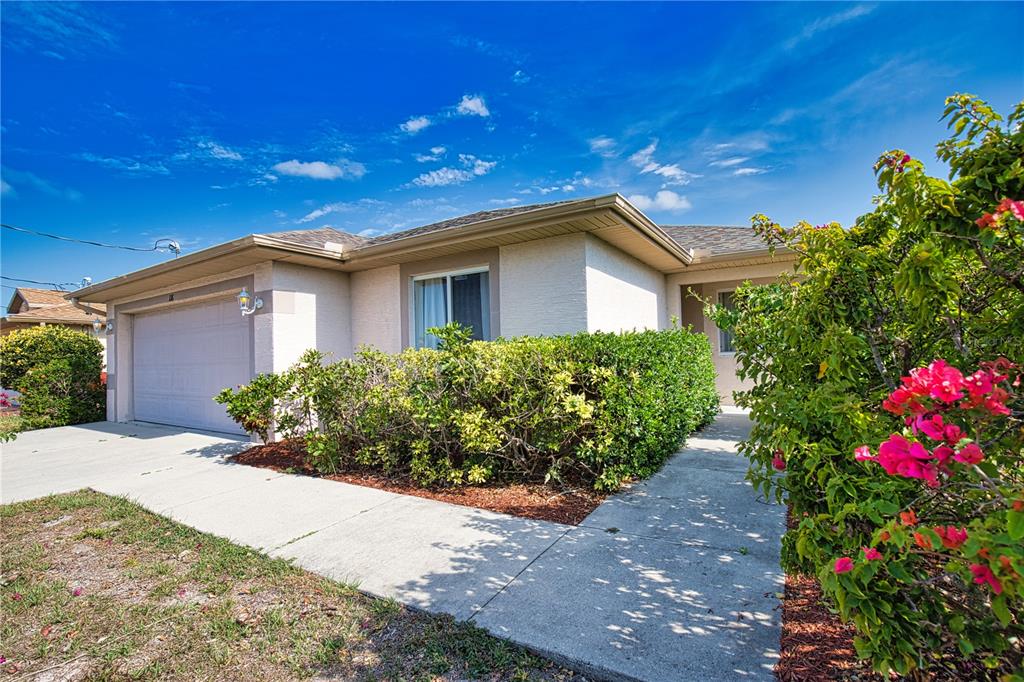 A single-story house with a garage, a concrete walkway, and landscaping under a blue sky — 116 ALBATROSS ROAD, ROTONDA WEST, FL