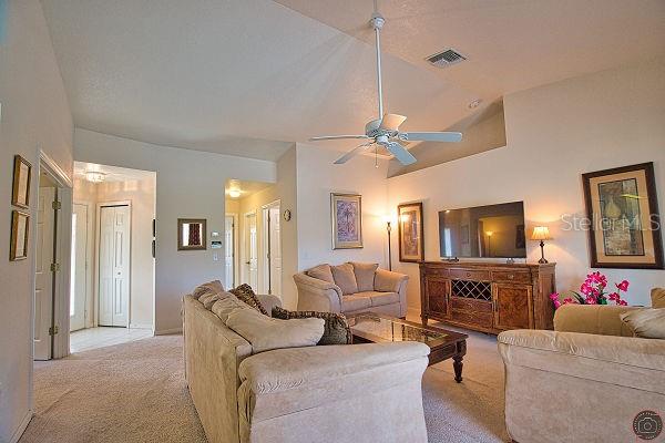 A living room features beige carpet, a ceiling fan, and a large television on a console — 116 ALBATROSS ROAD, ROTONDA WEST, FL