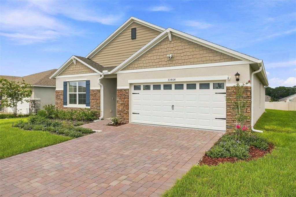 A single-story suburban house with a paver driveway, stone accents, and a two-car garage — 33464 COPPER HILL WAY, SORRENTO, FL