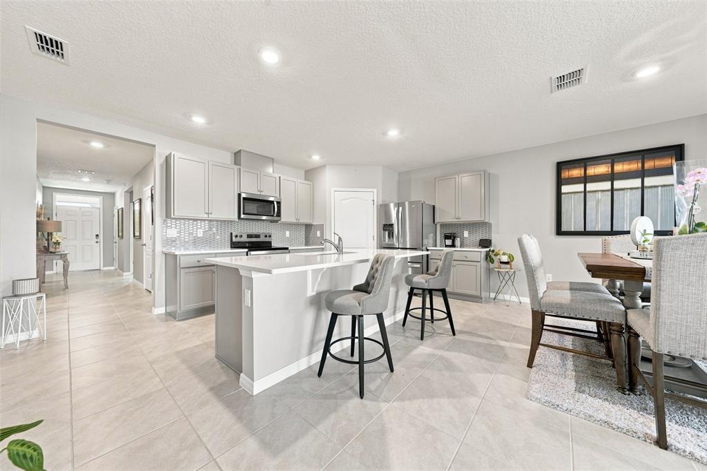 A modern kitchen features gray cabinets, a white island with bar stools, and tile flooring — 33464 COPPER HILL WAY, SORRENTO, FL