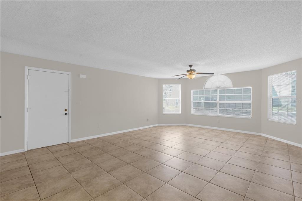 An empty living room with beige tile flooring, light-colored walls, and a ceiling fan — 2731 N POINCIANA BOULEVARD UNIT 107, KISSIMMEE, FL