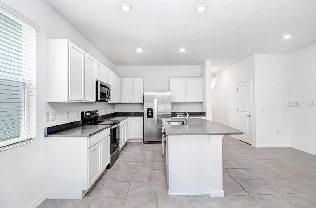 A modern kitchen features white cabinets, stainless steel appliances, a center island, and tile flooring — 398 MANGROVE SHADE CIRCLE, APOLLO BEACH, FL