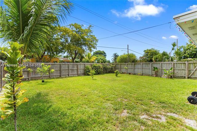 A grassy backyard features a wooden fence, a palm tree, and a small plant — 2407 Dewey St, Hollywood FL 33020, HOLLYWOOD, FL