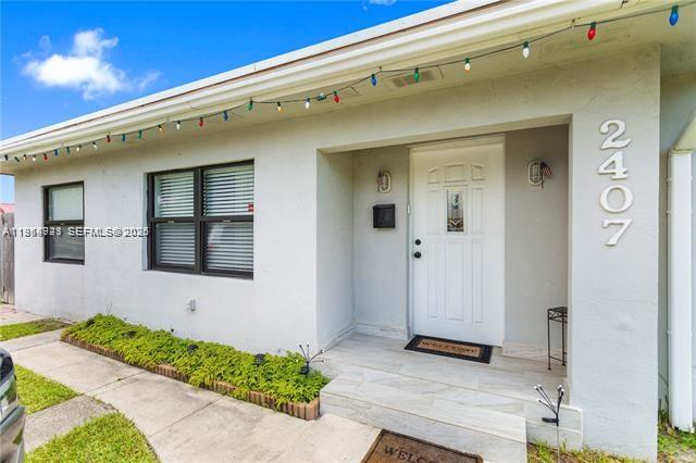 The exterior of a house features a white front door, a window, and string lights — 2407 Dewey St, Hollywood FL 33020, HOLLYWOOD, FL