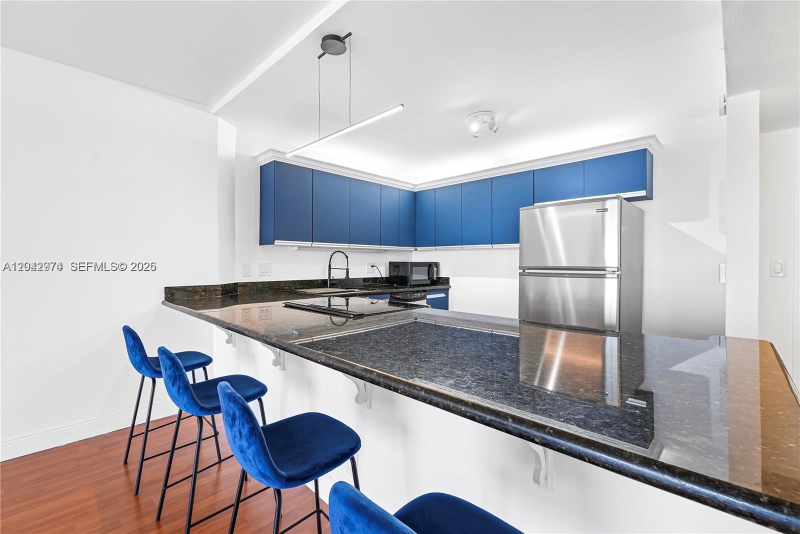 A kitchen features blue cabinets, dark granite countertops, and blue bar stools — 2500 Parkview Dr # 1503, Hallandale Beach FL 33009, HALLANDALE BEACH, FL