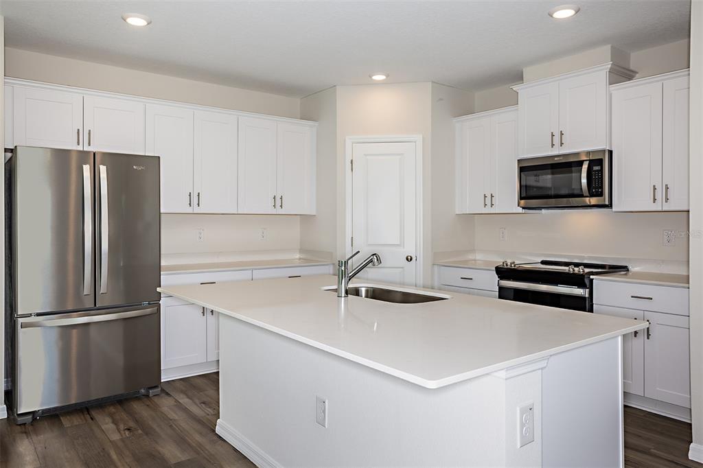 A modern kitchen features white cabinetry, stainless steel appliances, a center island, and wood-look flooring — 9144 BENT BRANCH, DADE CITY, FL