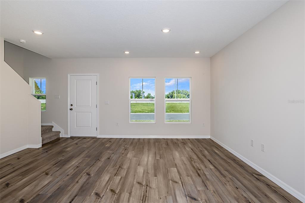 A living room with wood-look flooring, recessed lighting, two windows, and a staircase — 9144 BENT BRANCH, DADE CITY, FL