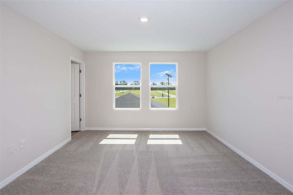 An empty bedroom features light-colored walls, gray carpeting, and two windows overlooking a grassy field — 9144 BENT BRANCH, DADE CITY, FL