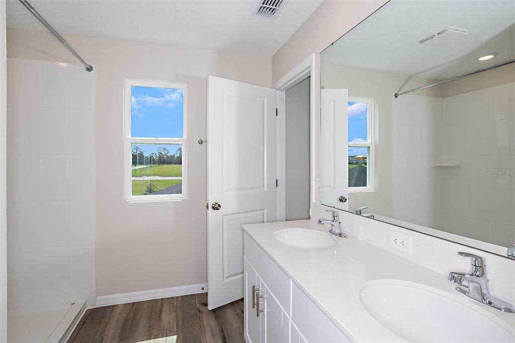 A bathroom features a double vanity with white cabinets, a mirror, and a walk-in shower — 9144 BENT BRANCH, DADE CITY, FL