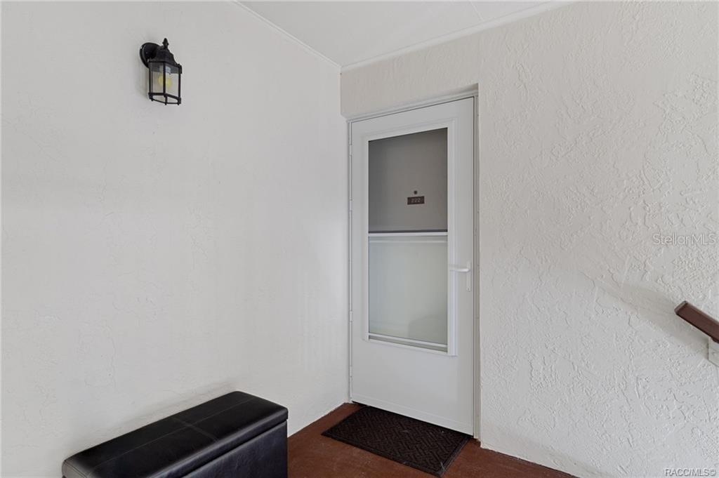 A white exterior door with a glass panel is set into a textured white wall — 2400 FOREST DRIVE UNIT 221, INVERNESS, FL