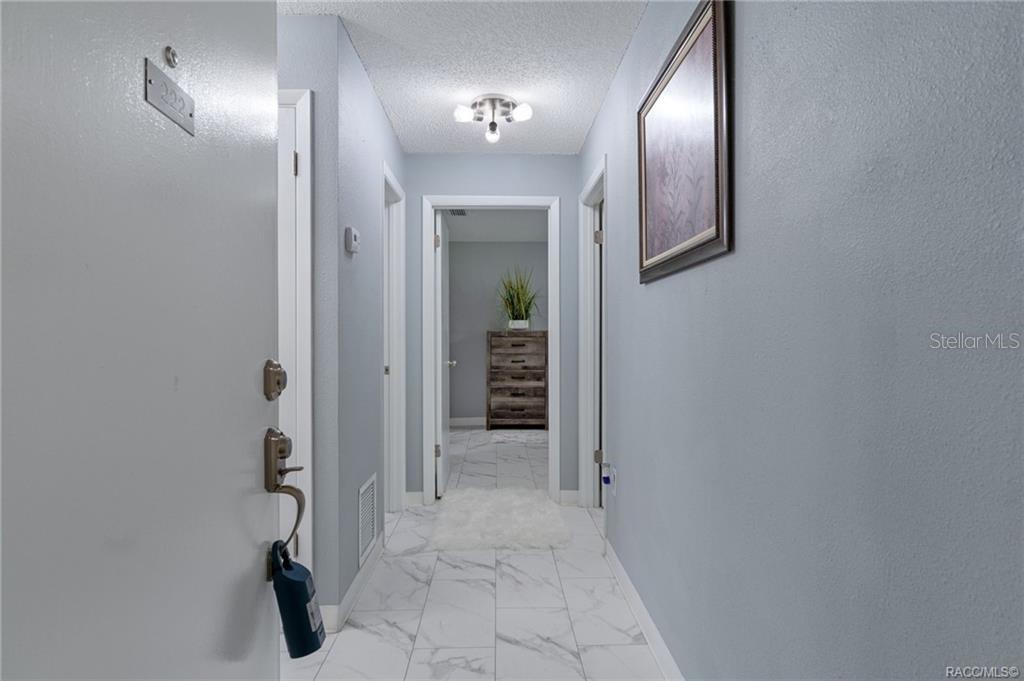 A hallway with white marble-look tile flooring leads to a doorway with a wooden dresser — 2400 FOREST DRIVE UNIT 221, INVERNESS, FL