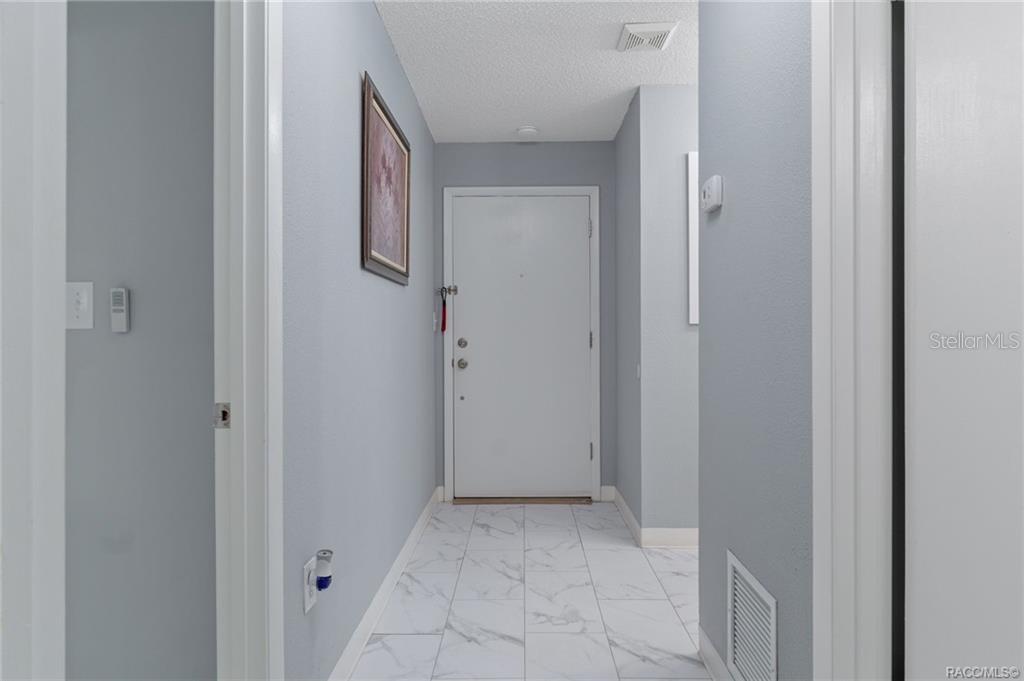 A hallway with light gray walls, white trim, and white marble-look tile flooring — 2400 FOREST DRIVE UNIT 221, INVERNESS, FL
