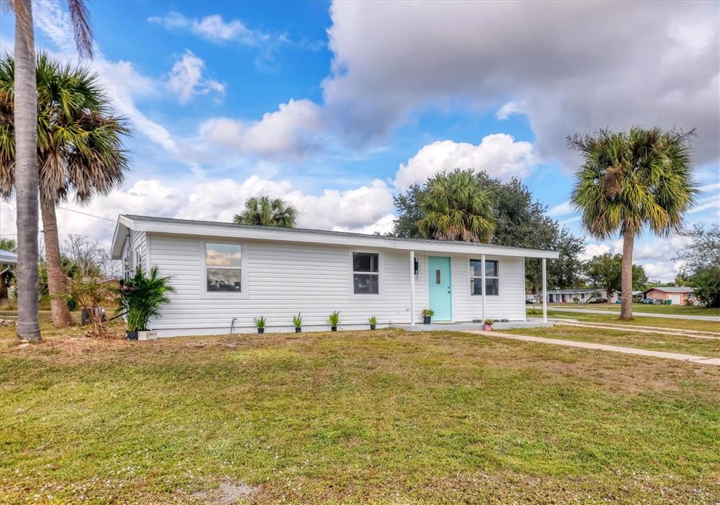 A white single-story house with a light blue front door stands under a cloudy sky — 22152 LARAMORE AVENUE, PORT CHARLOTTE, FL