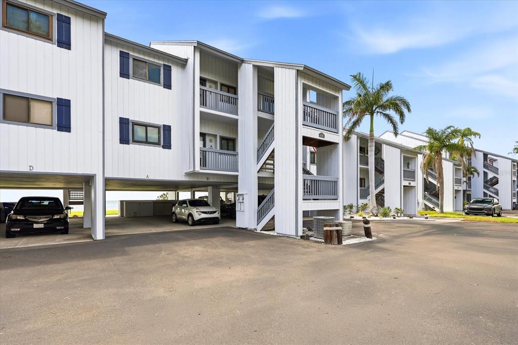 A multi-story white apartment building with covered parking on the ground level and palm trees — 818 BAHIA DEL SOL DRIVE UNIT 28, RUSKIN, FL