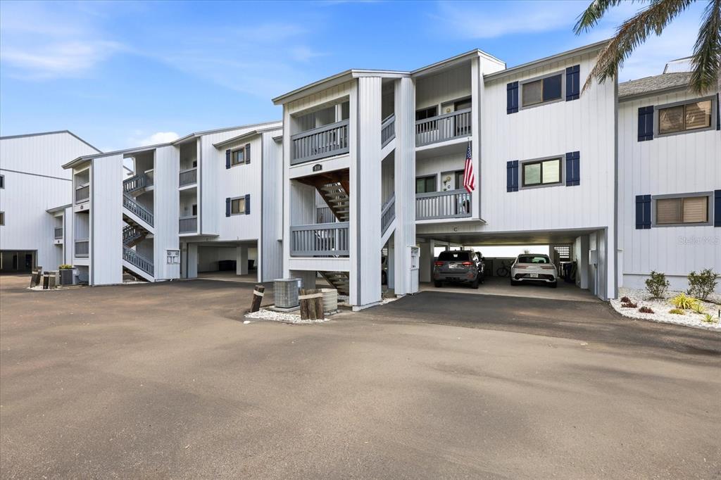 A three-story apartment building with white siding, blue shutters, and covered parking on the ground level — 818 BAHIA DEL SOL DRIVE UNIT 28, RUSKIN, FL