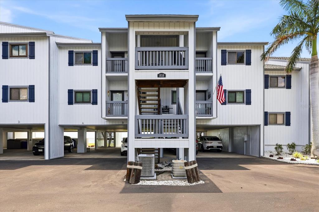 A three-story apartment building with elevated parking and a central staircase under a blue sky — 818 BAHIA DEL SOL DRIVE UNIT 28, RUSKIN, FL