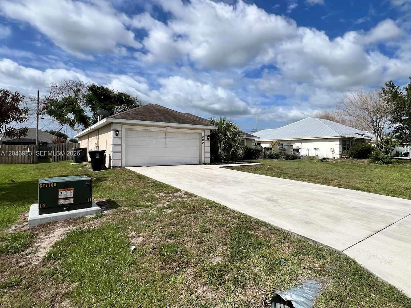A single-story house with a white garage door, concrete driveway, and a green utility box — PORT ST. LUCIE, FL