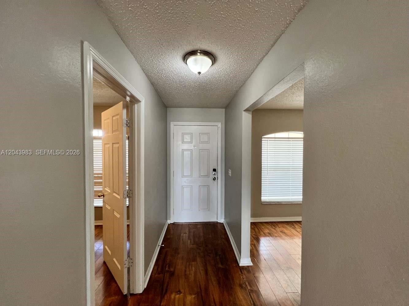 A hallway with wood-look flooring leads to a white front door and a side room — PORT ST. LUCIE, FL