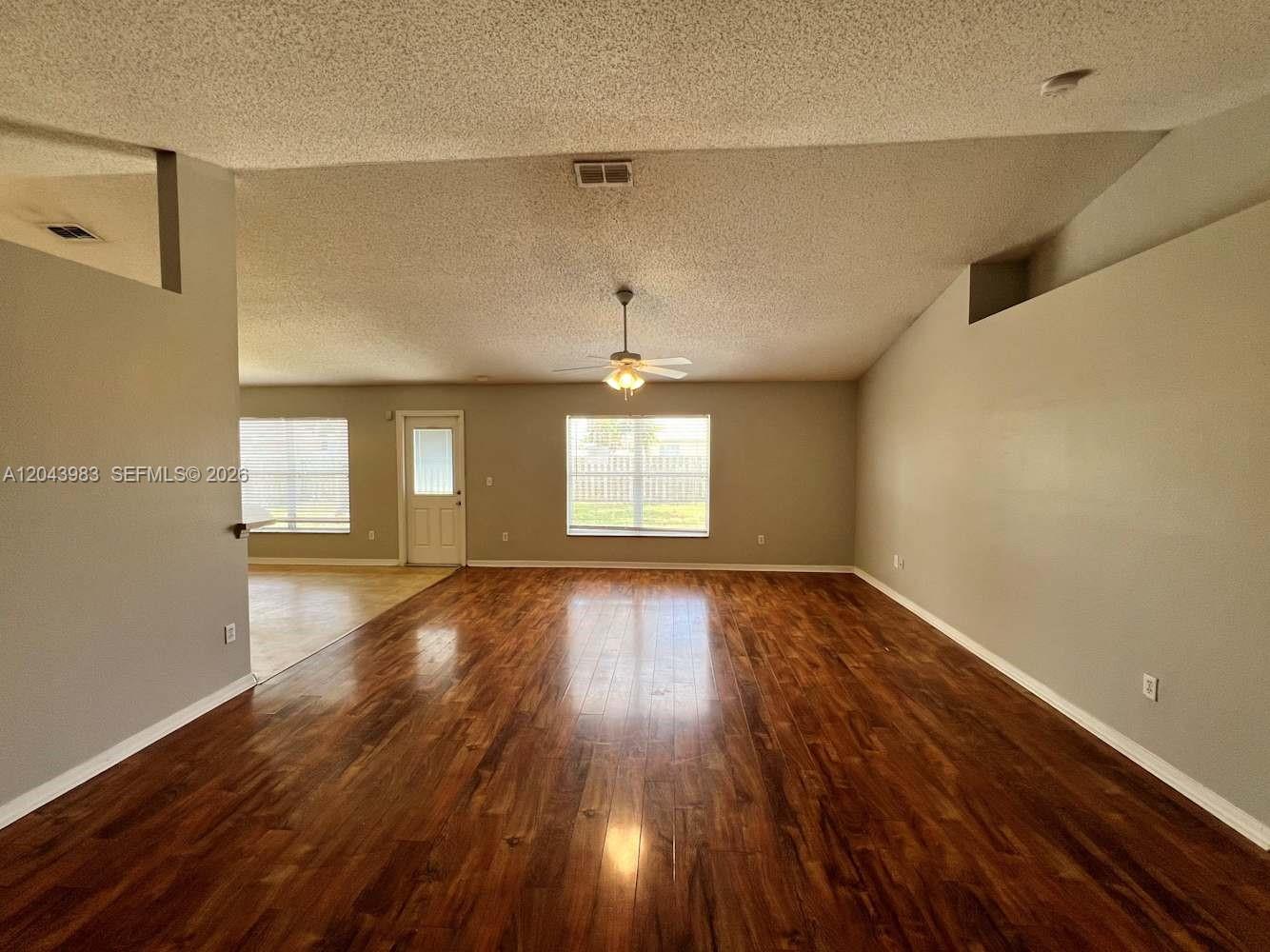 A spacious living room features wood-look flooring, a ceiling fan, and vaulted ceilings — PORT ST. LUCIE, FL