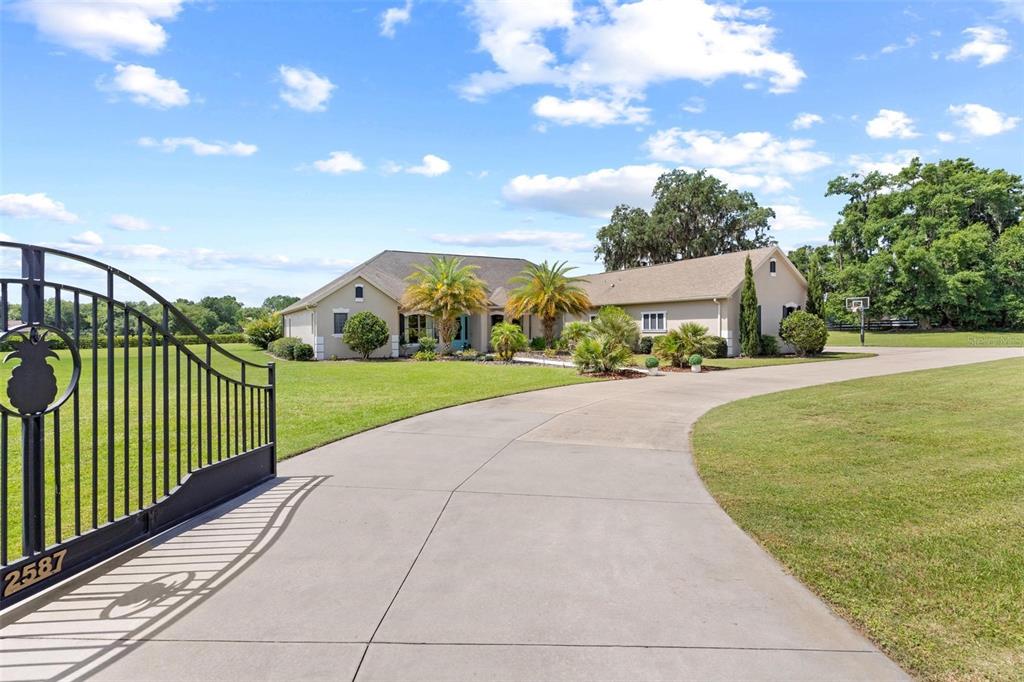 A paved driveway leads to a single-story house with palm trees and a gated entrance — 2587 NE 108TH LANE, OXFORD, FL