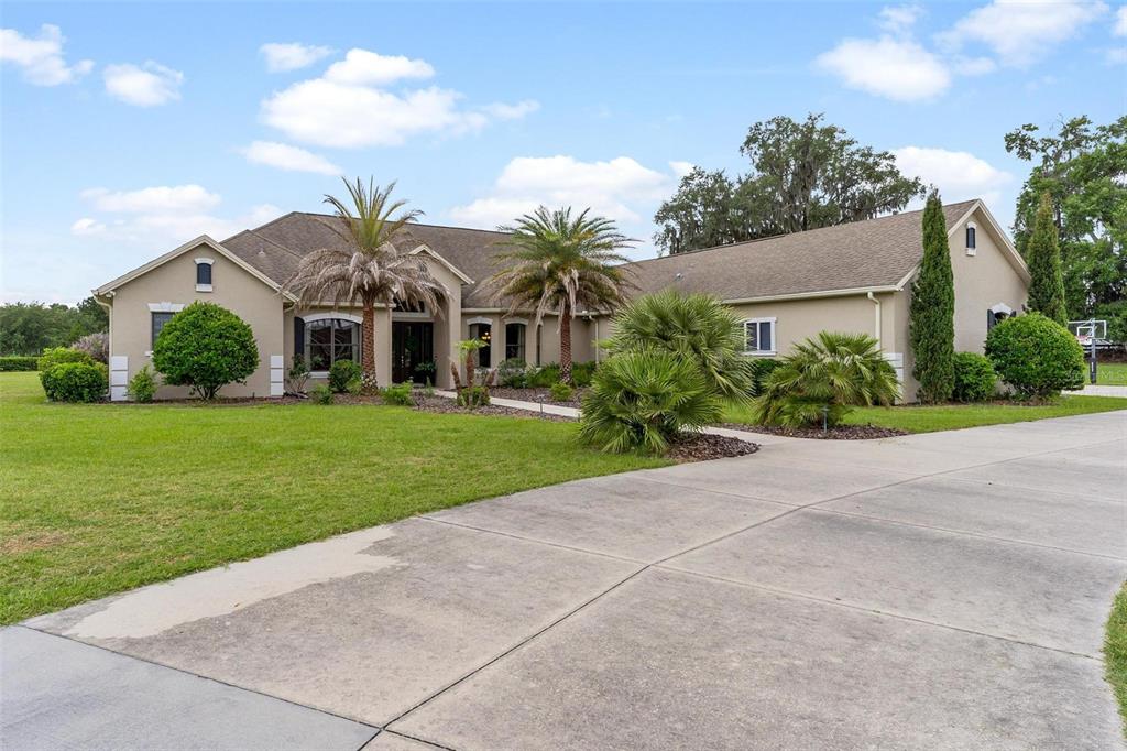 A single-story beige house with a concrete driveway, palm trees, and a green lawn — 2587 NE 108TH LANE, OXFORD, FL