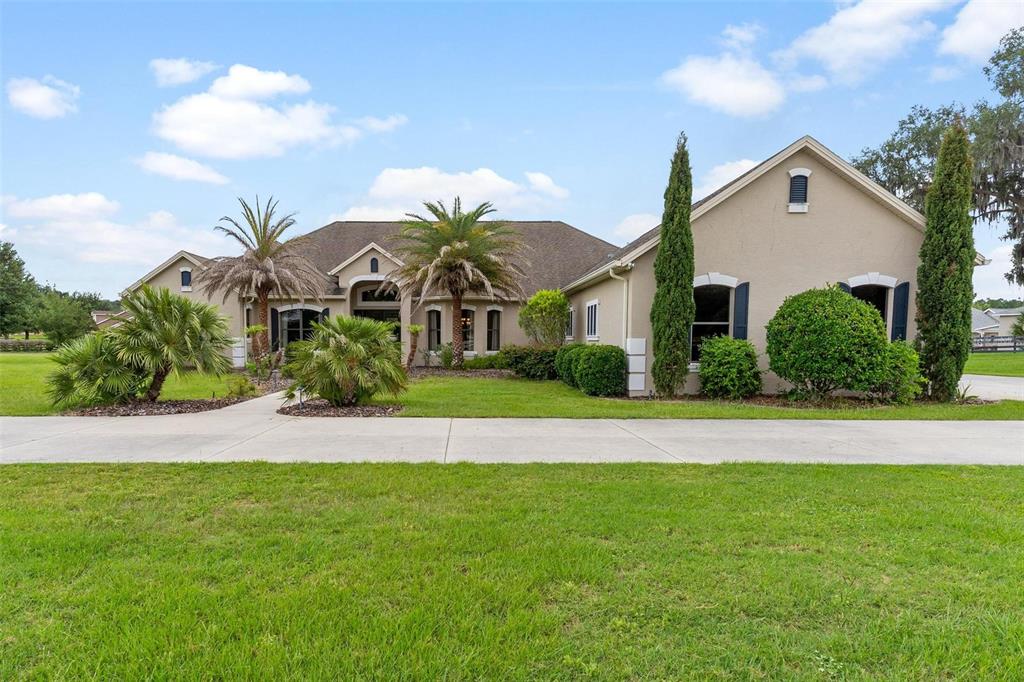 A single-story tan house with a concrete driveway, palm trees, and manicured landscaping — 2587 NE 108TH LANE, OXFORD, FL