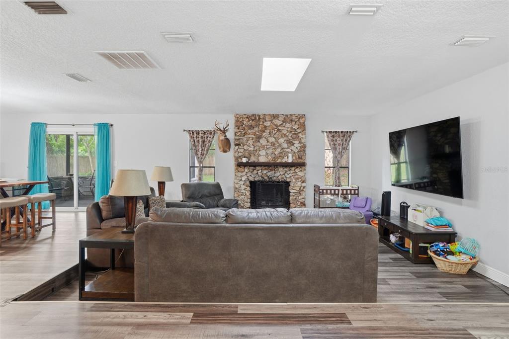 A living room features a stone fireplace, a large television, and wood-look flooring — 2700 CONCORD ROAD, DELAND, FL