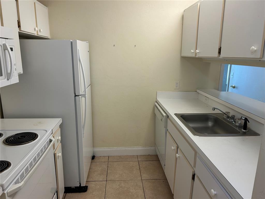 A kitchen features white cabinets, white appliances, a stainless steel sink, and tiled flooring — 3800 SW 20TH AVENUE UNIT 501, GAINESVILLE, FL