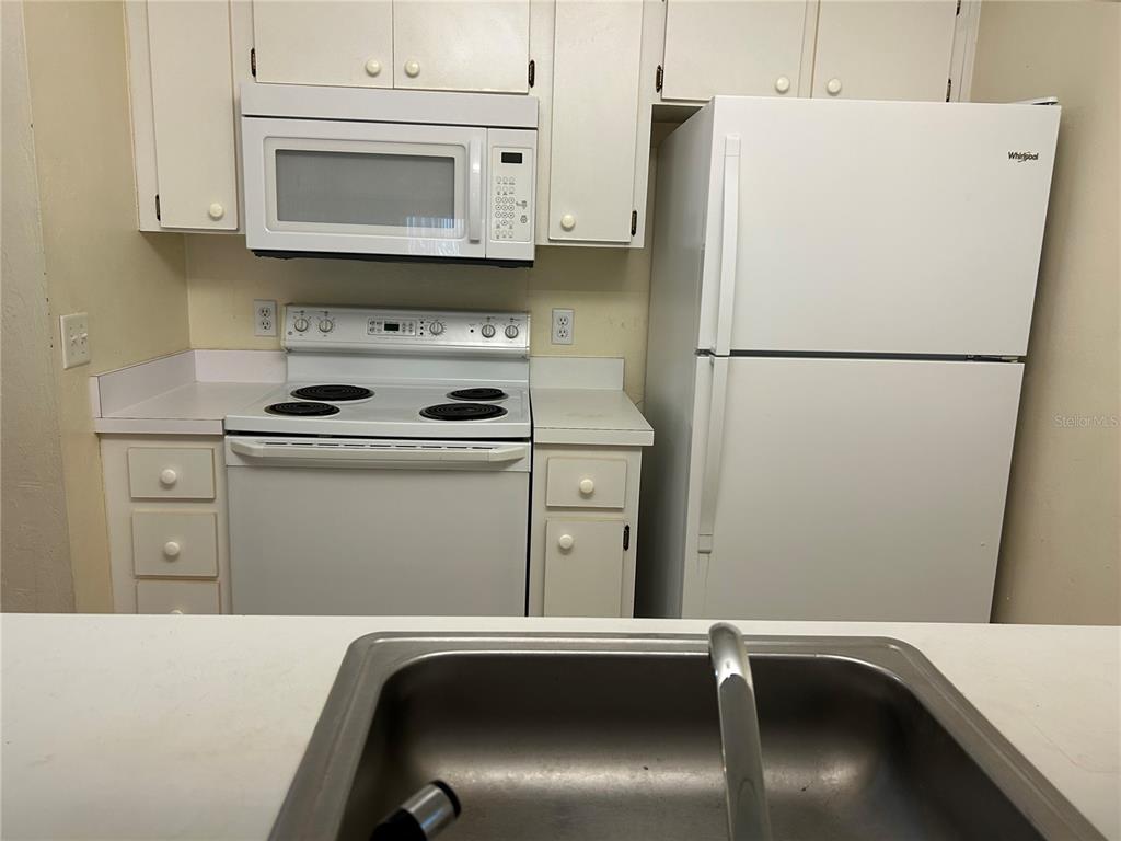 A kitchen features white cabinets, a white electric stove, a microwave, and a white refrigerator — 3800 SW 20TH AVENUE UNIT 501, GAINESVILLE, FL
