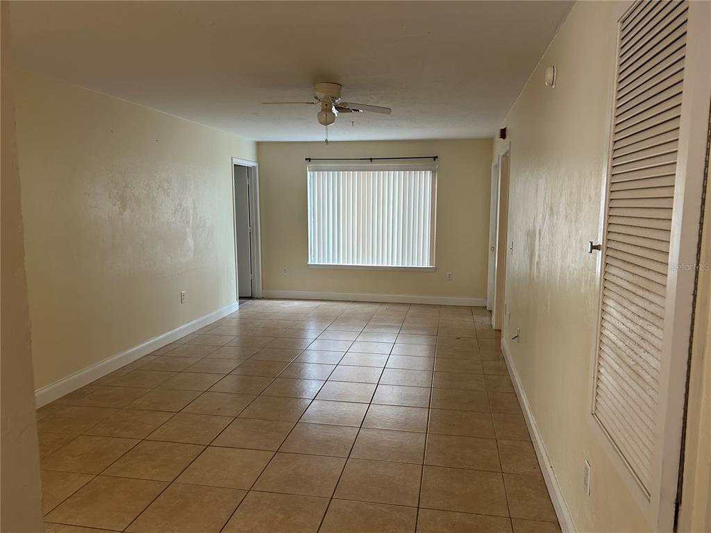 An empty room with beige tile flooring, a ceiling fan, and a large window — 3800 SW 20TH AVENUE UNIT 501, GAINESVILLE, FL