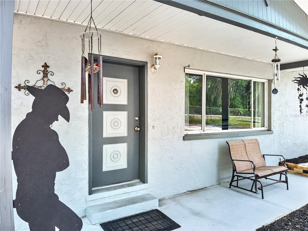 A gray front door with three square windows sits on a covered concrete porch — 5304 TILLMAN ROAD, LAKELAND, FL