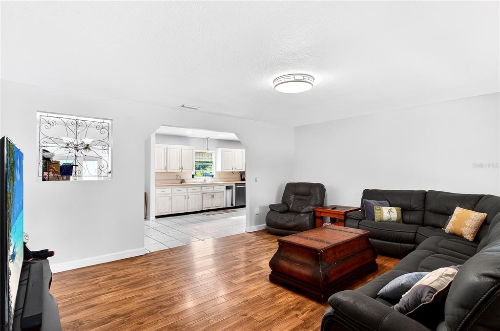 A living room with wood-look flooring and a sectional sofa opens into a white kitchen — 5304 TILLMAN ROAD, LAKELAND, FL