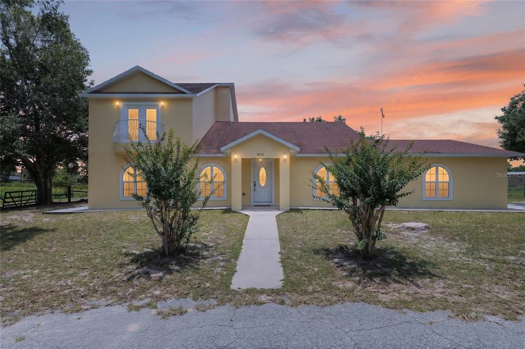 A two-story yellow house with a front walkway and arched windows at sunset — 3830 GRIFFIN VIEW DRIVE, LADY LAKE, FL