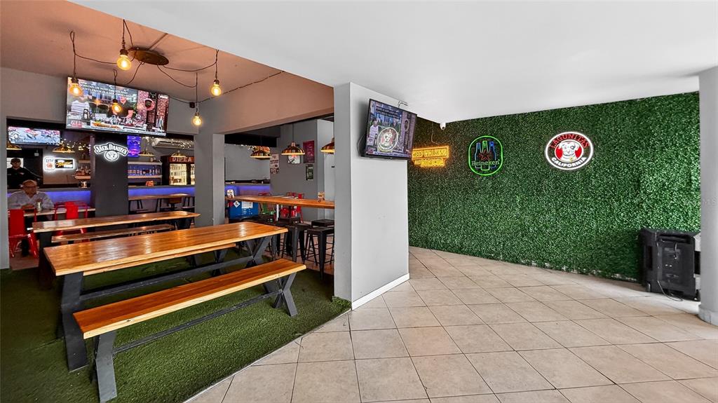 A bar interior features wooden tables, artificial grass flooring, and a green wall with signage — 133 O'NEILL ROAD, SAN JUAN, PR