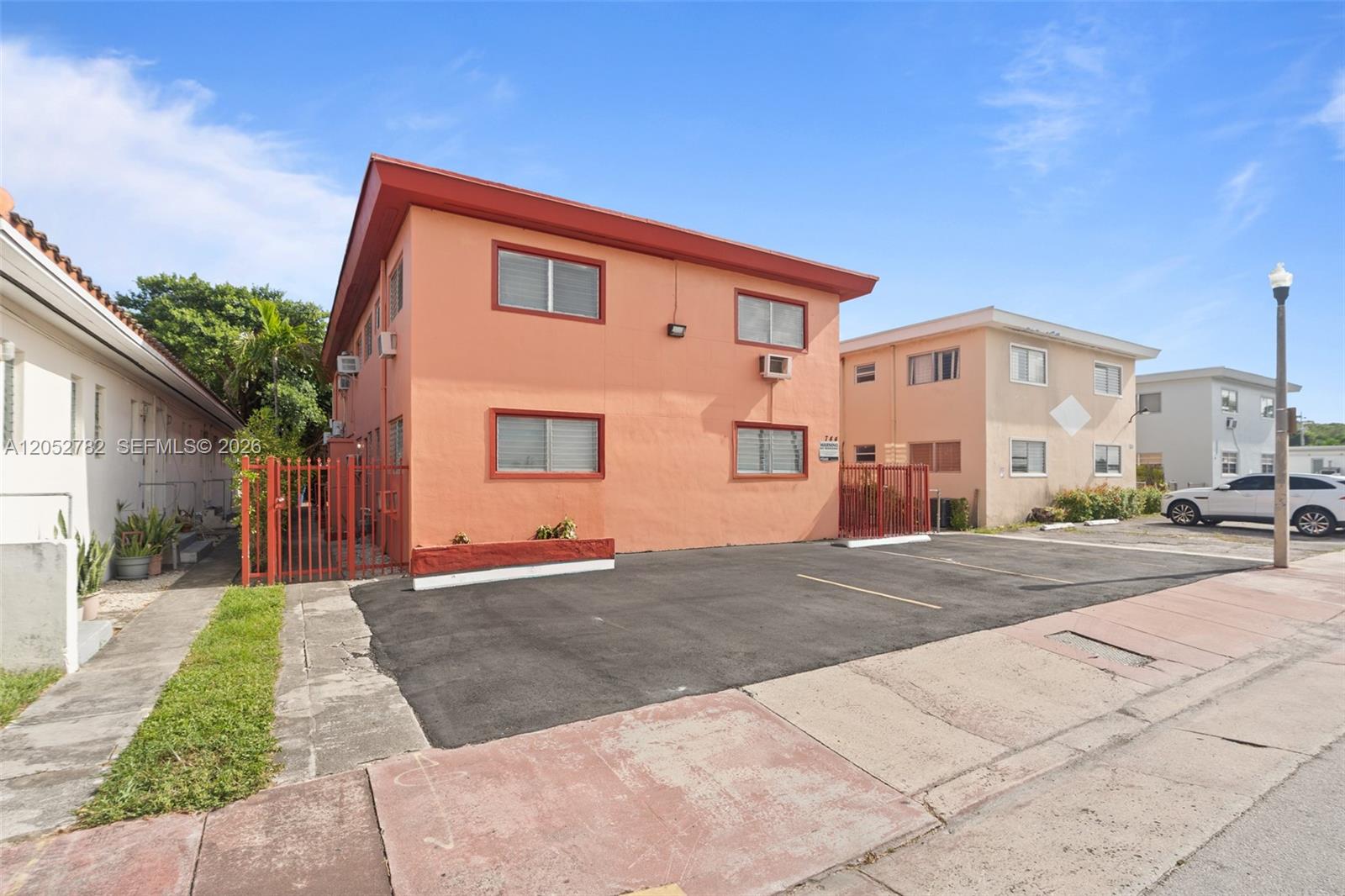 A two-story peach-colored apartment building features a paved parking lot and red metal fencing — 744 85th St, Miami Beach FL 33141, MIAMI BEACH, FL
