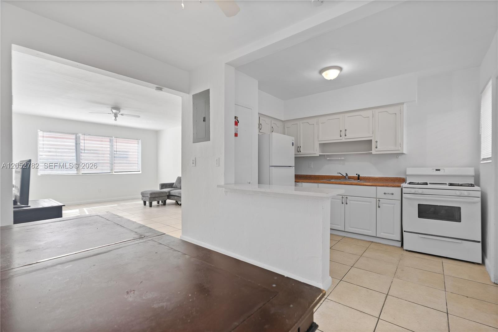 A kitchen with white cabinets and appliances opens into a living area with tile floors — 744 85th St, Miami Beach FL 33141, MIAMI BEACH, FL