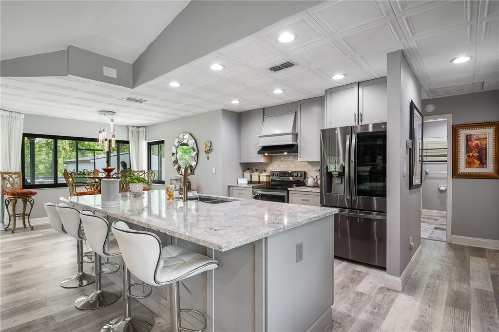 A kitchen features a granite island with bar stools, stainless steel appliances, and coffered ceilings — 2044 TUNISIA AVENUE, SPRING HILL, FL