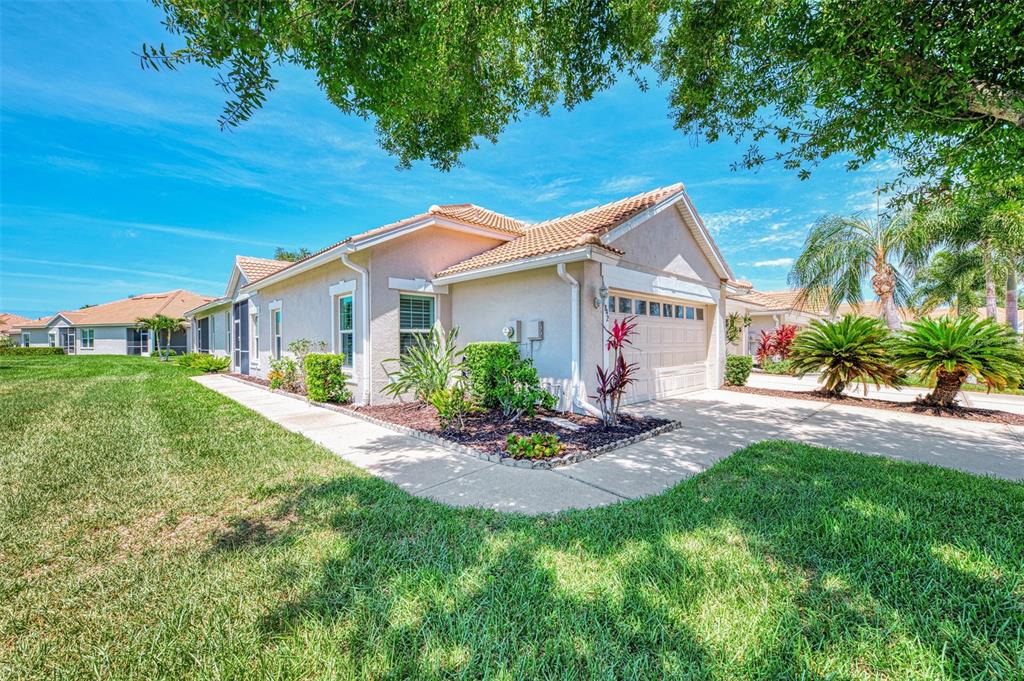 A beige single-story house with a two-car garage and a landscaped front yard — 1842 SAN SILVESTRO DRIVE, VENICE, FL