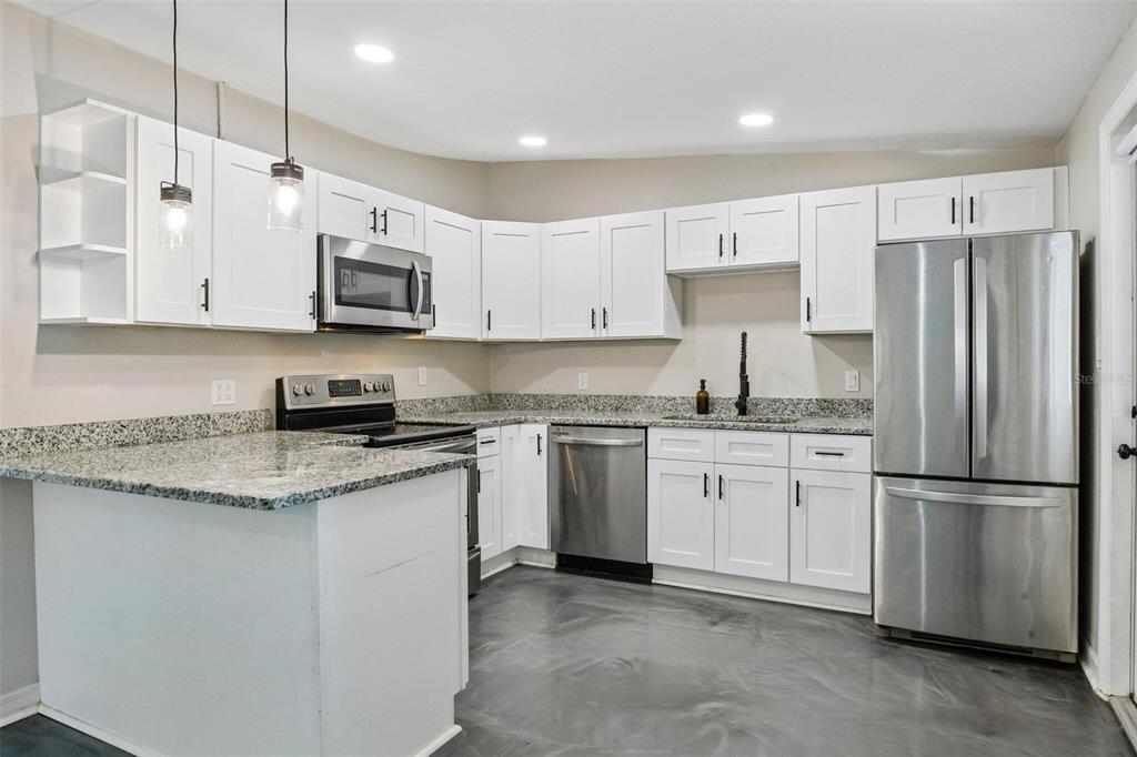A kitchen with white cabinets, granite countertops, stainless steel appliances, and gray flooring — 2416 EMORY AVENUE, BRADENTON, FL