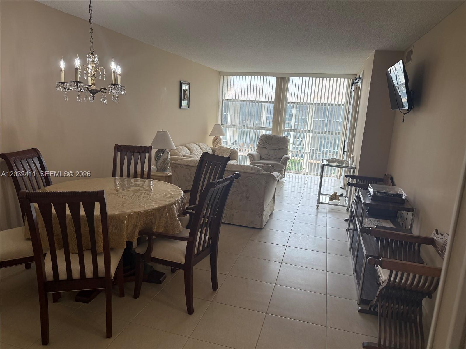 A dining area with a chandelier and a living room with tile floors and balcony access — 851 Three Islands Blvd # 511, Hallandale Beach FL 33009, HALLANDALE BEACH, FL