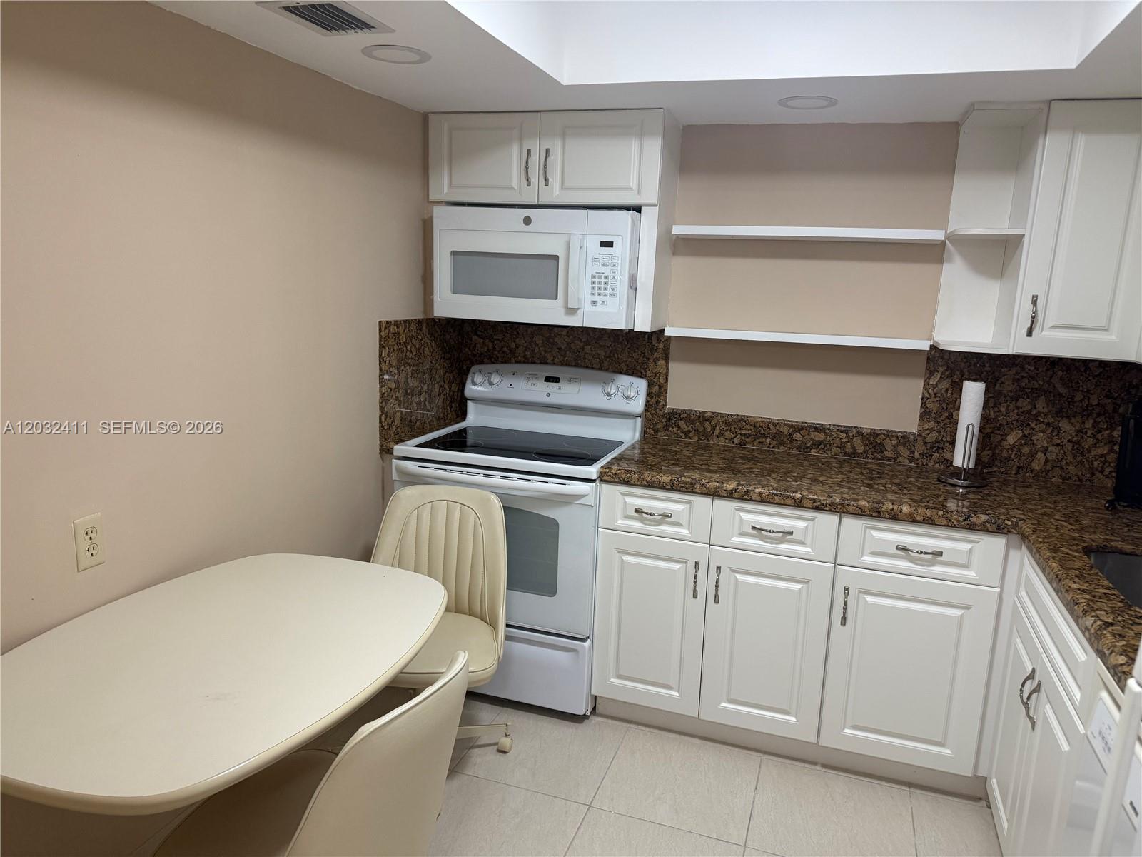 A kitchen features white cabinets, a white stove, a microwave, and a small dining table — 851 Three Islands Blvd # 511, Hallandale Beach FL 33009, HALLANDALE BEACH, FL