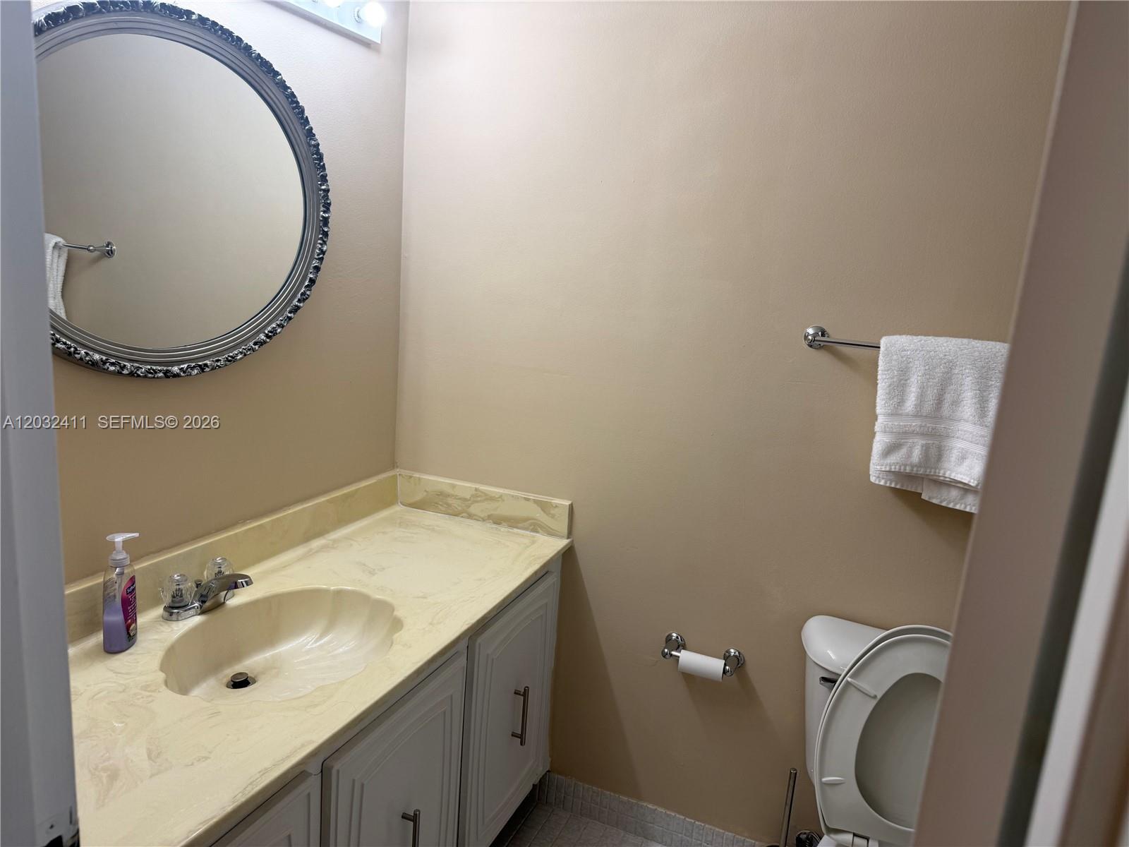 A bathroom features a vanity with a shell-shaped sink, a round mirror, and a toilet — 851 Three Islands Blvd # 511, Hallandale Beach FL 33009, HALLANDALE BEACH, FL