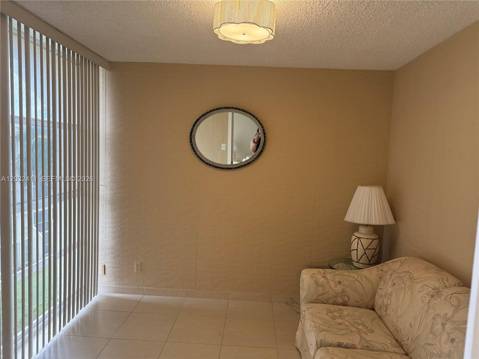A room with beige walls, tile flooring, a floral sofa, and a round wall mirror — 851 Three Islands Blvd # 511, Hallandale Beach FL 33009, HALLANDALE BEACH, FL